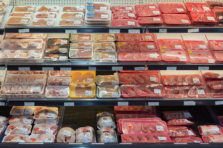 Trays of pork, beef and chicken laid out under the lights of a supermarket meat counter.