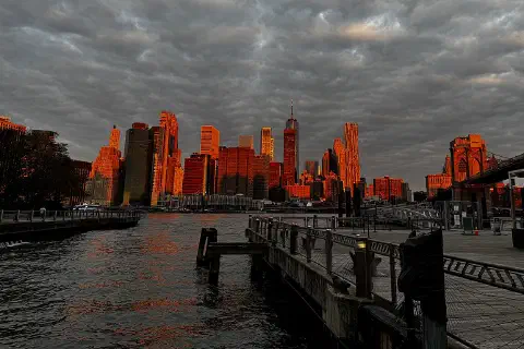 The Manhattan Financial District skyline under an orange sky, seen from Brooklyn Bridge Park.